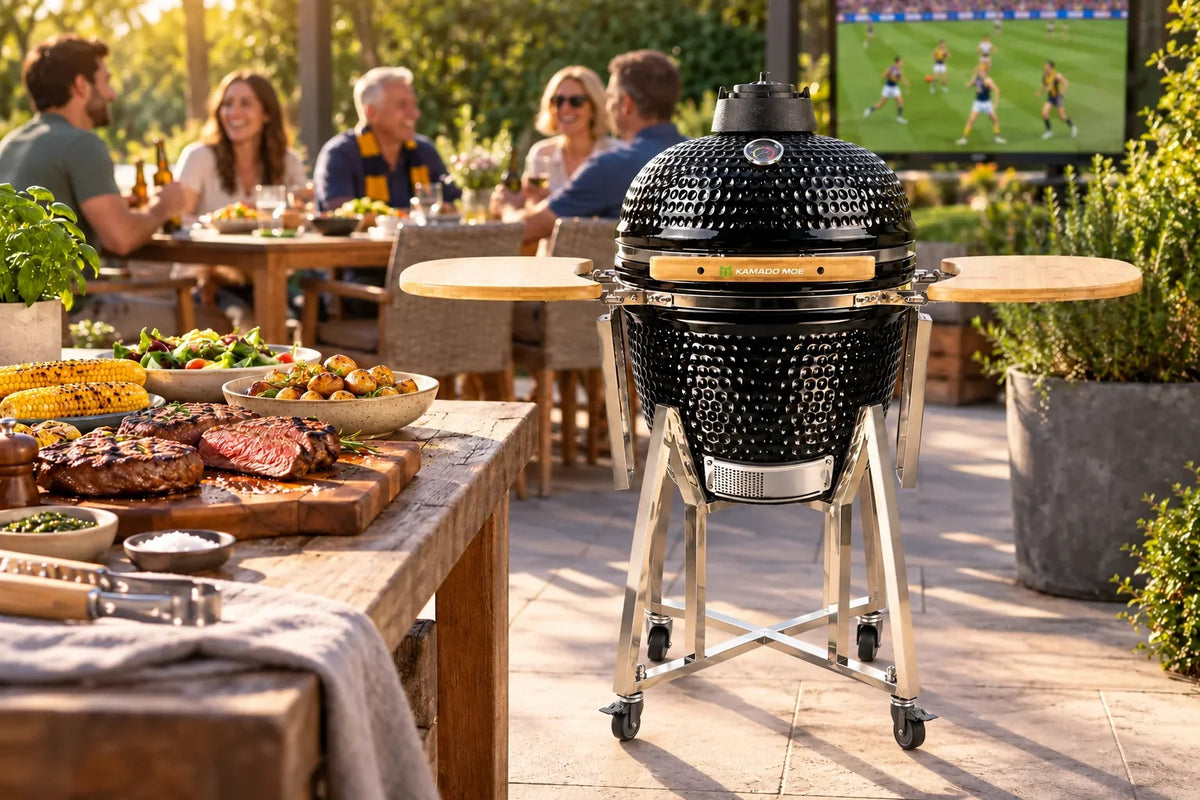 Lifestyle illustration of the black Kamado Moe Classic 18-inch barbecue beside chargrilled steak during an outdoor AFL gathering.
